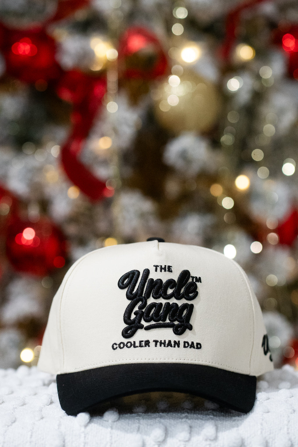 White cap with 'The Uncle Gang Cooler Than Dad' text in front of a decorated Christmas tree.