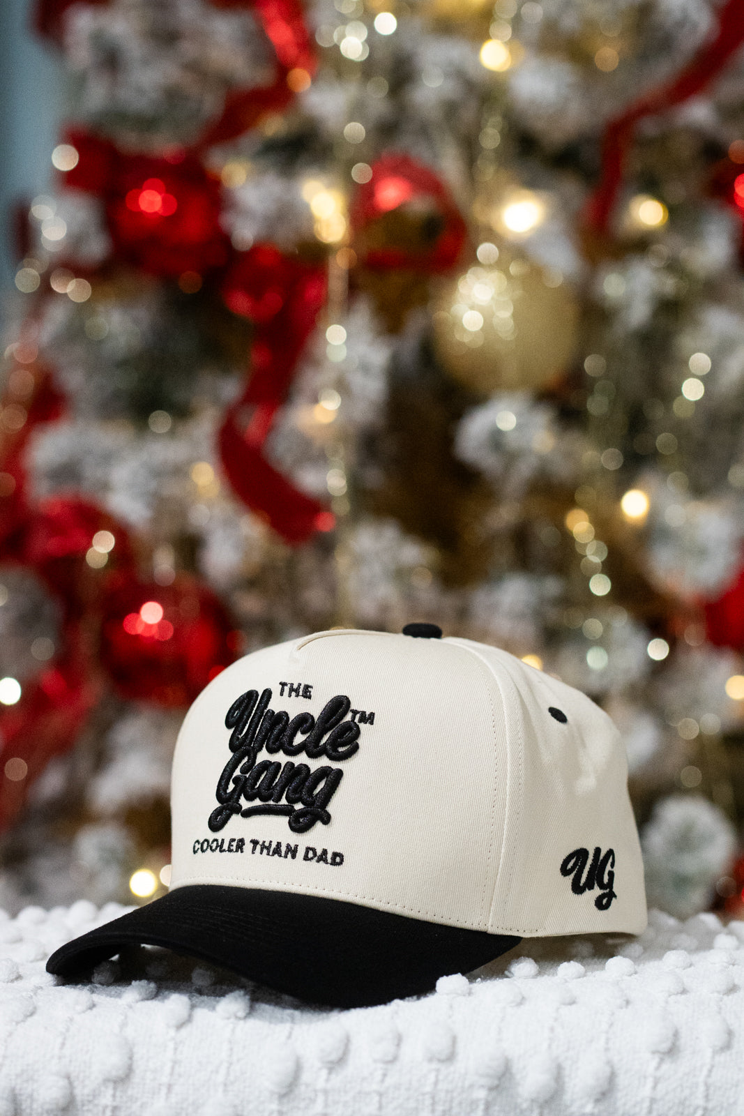 White cap with black text in front of a decorated Christmas tree