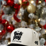 White cap with black text in front of a decorated Christmas tree