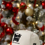 Beige cap with text in front of a decorated Christmas tree
