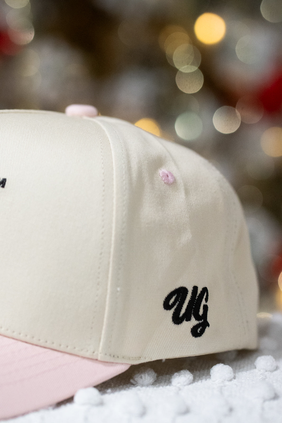 Beige and pink cap with 'UG' logo on a blurred background