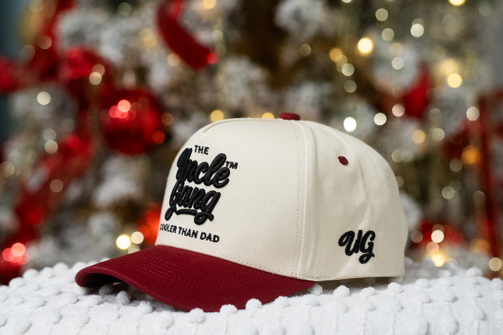 Cap with 'The Uncle Gang' logo on a snowy surface with blurred festive lights in the background