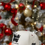 White and red cap with text in front of a decorated Christmas tree