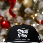 Black cap with 'The Uncle Gang Cooler Than Dad' text in front of a decorated Christmas tree.