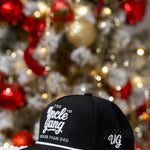 Black cap with text in front of a decorated Christmas tree