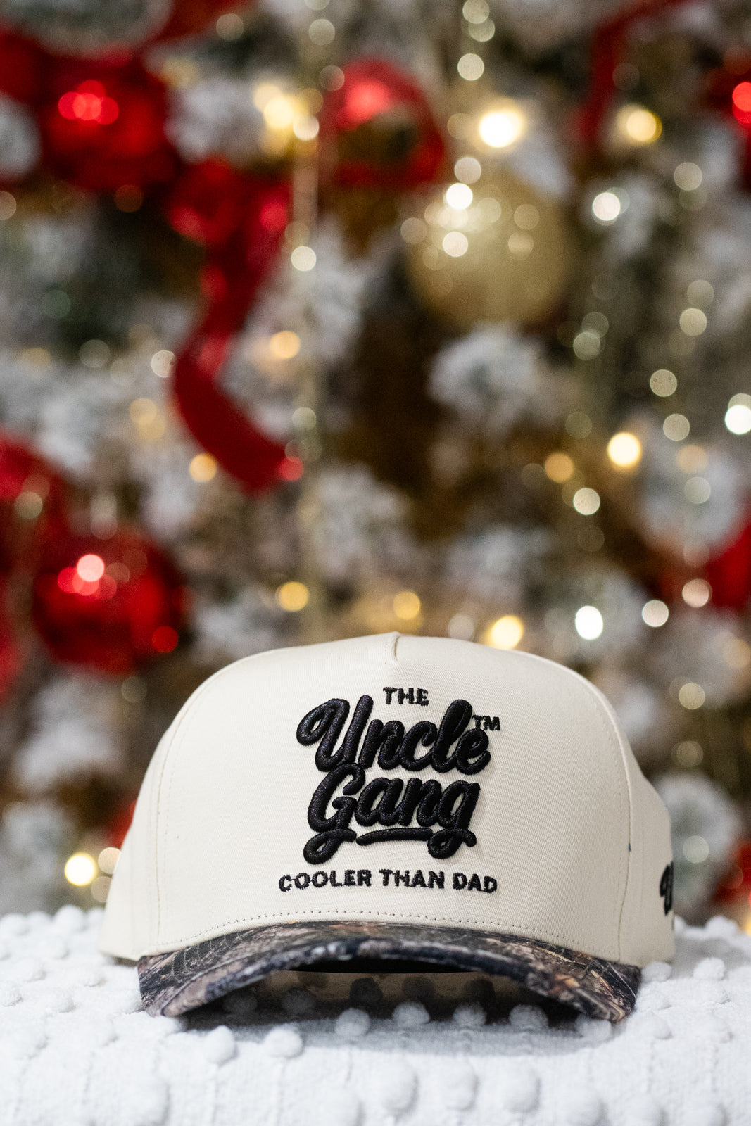 White cap with 'The Uncle Gang Cooler Than Dad' text in front of a decorated Christmas tree.