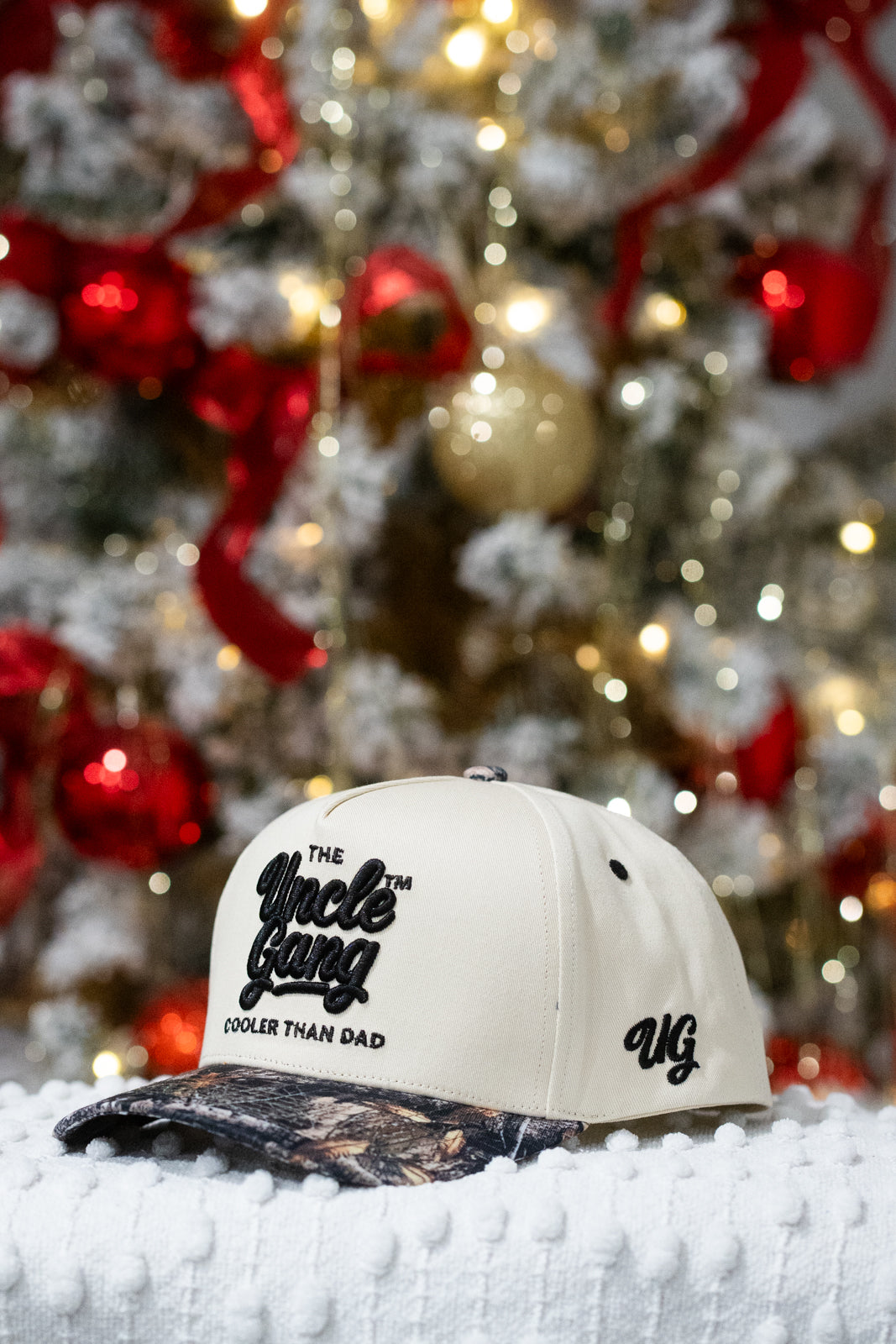 White cap with 'The Uncle Gang' logo in front of a decorated Christmas tree.