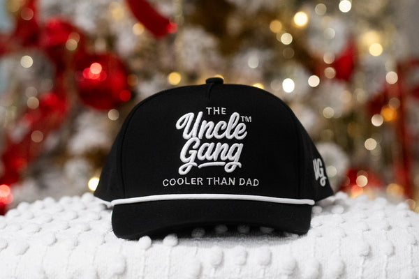 Black cap with 'The Uncle Gang' text on a textured surface with blurred festive background