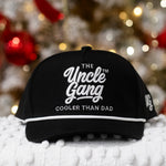 Black cap with 'The Uncle Gang' text on a textured surface with blurred festive background