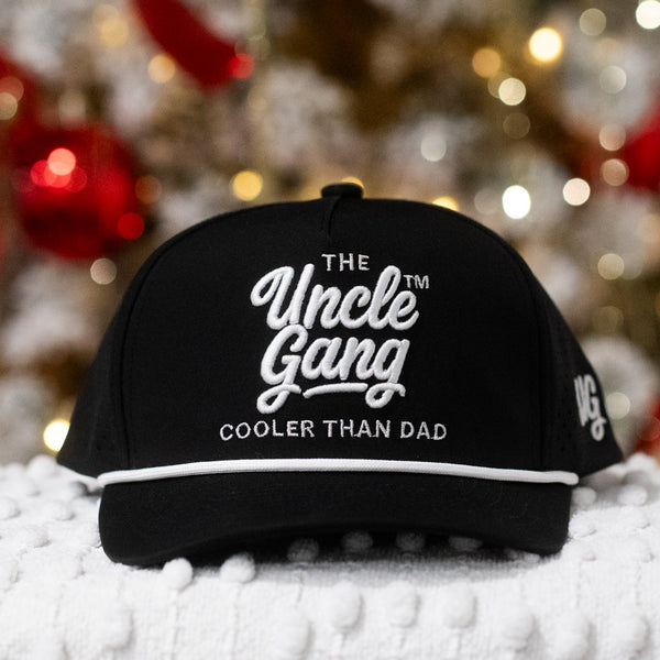 Black cap with 'The Uncle Gang' text on a textured surface with blurred festive background